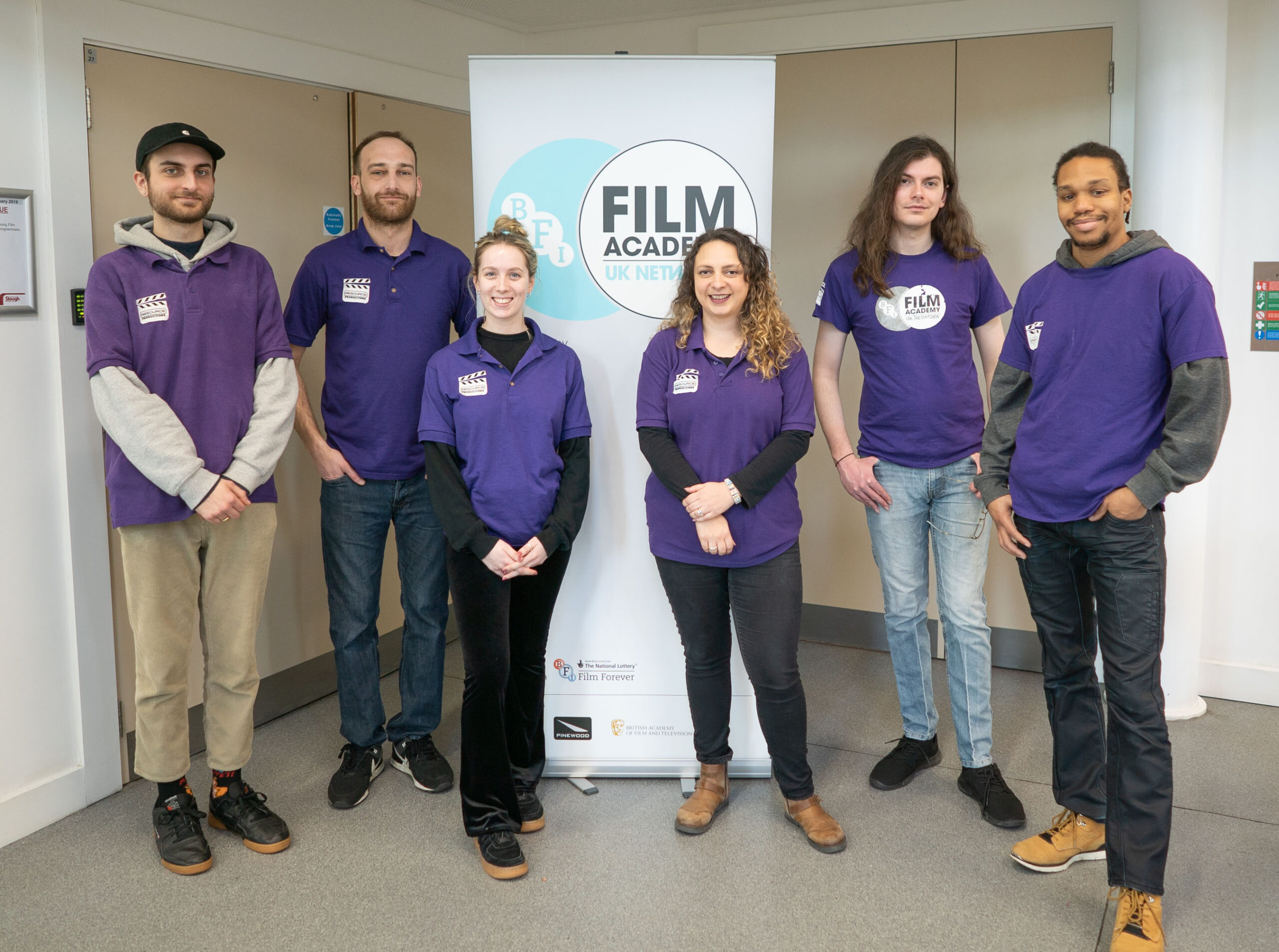 group of young people in purple BFI Film Academy T-shirts stand in front of a marketing banner.