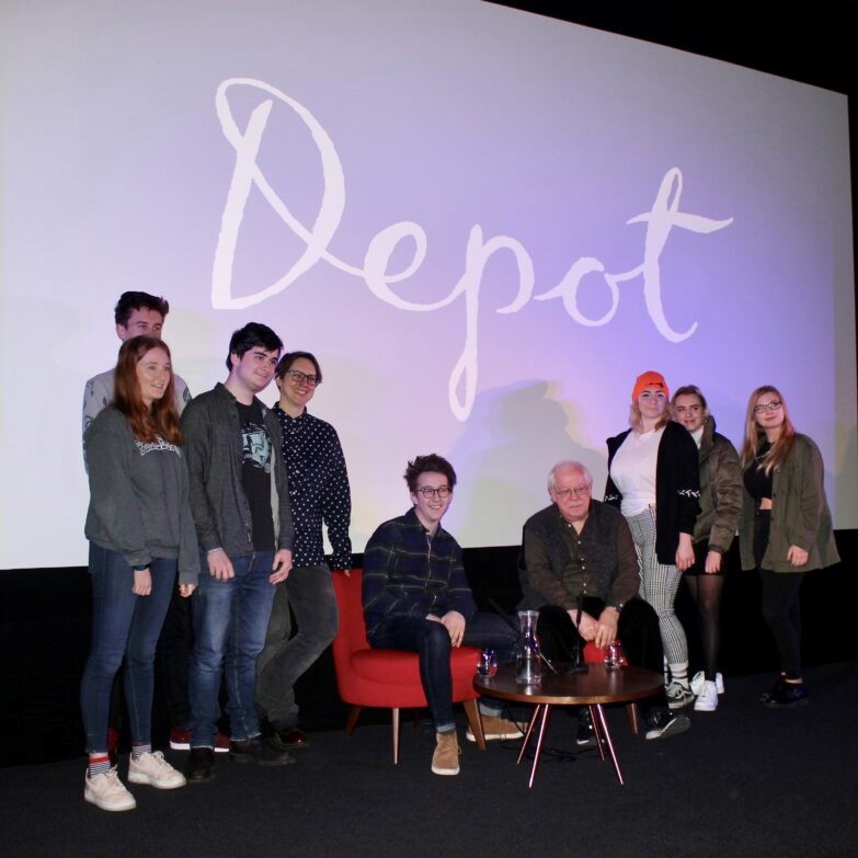 Group of young people and facilitator pose in front of a cinema screen with the Depot logo on it.