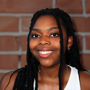 A young person with long dark braided hair and brown eyes, smiling.