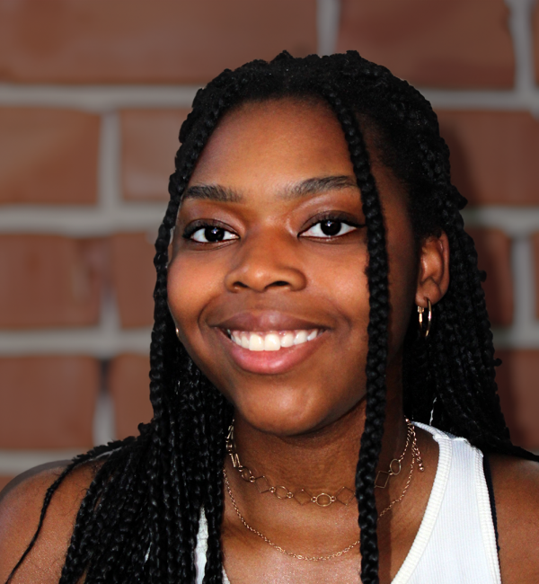 A young person with long dark braided hair and brown eyes, smiling.