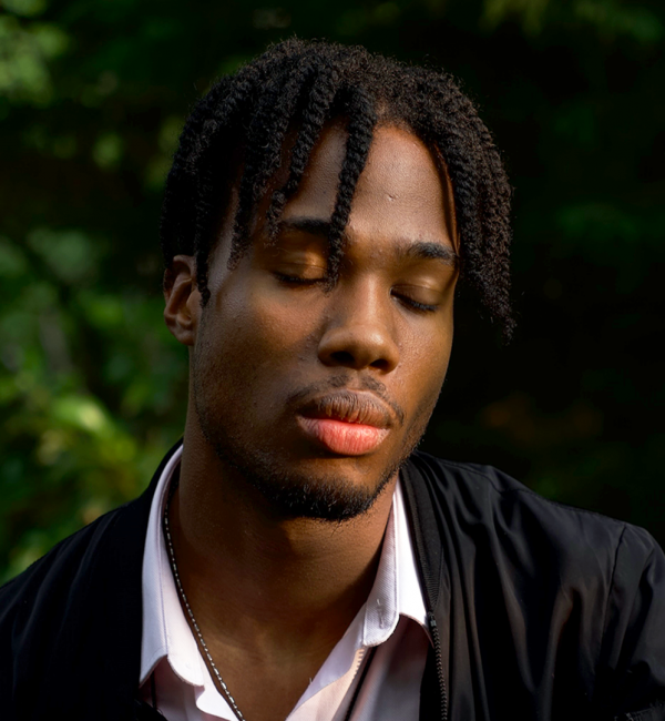 Short Cut Film Fund 3 – Chris Brown (no graphics) A young person with short braided hair and stubble. Their eyes are closed.